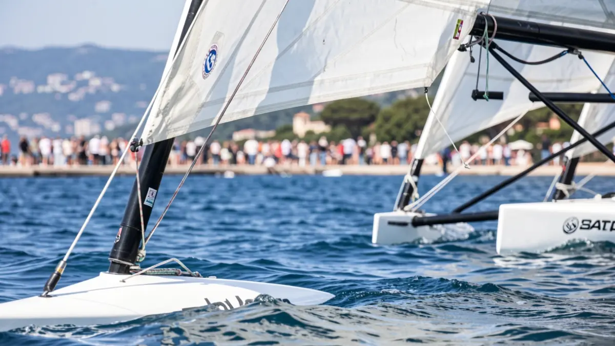 Primer plano de un velero Patín a Vela con el mar y la costa de fondo.